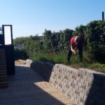 Anlægsgartner arbejder i et bed ved en nyopført støttemur af betonsten og en trappe ved en terrasse