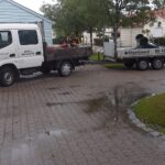Lille lastbil med lad og en trailer med minigraver parkeret på en indkørsel
