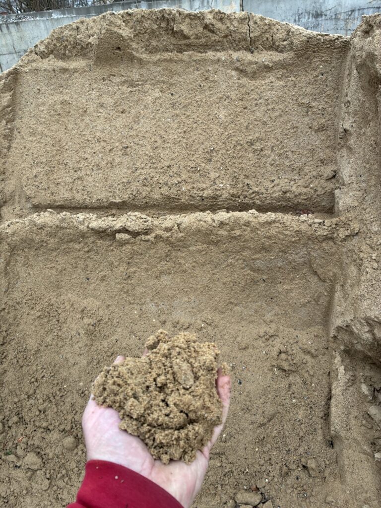 Hånd med en håndfuld sand foran en bunke sand